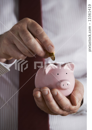 Businessman Putting Coin Into Piggy Bank Businessman Putting Coin Into Piggy Bank 13361419