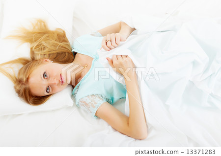 girl in nightshirt lying on white sheet in bed at home 13371283