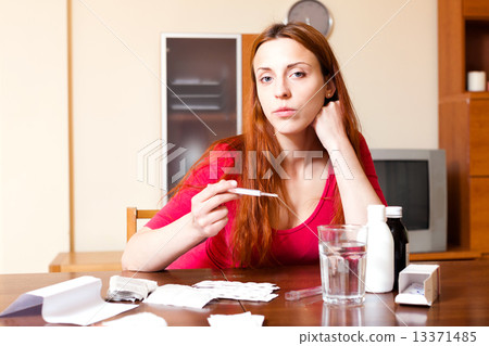 Sick ordinary woman looks by thermometer at home 13371485