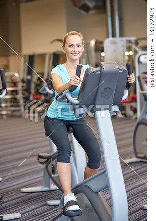 smiling woman exercising on exercise bike in gym smiling woman exercising on exercise bike in gym 13372923