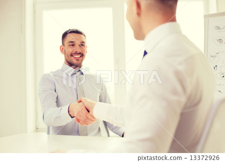 two smiling businessmen shaking hands in office 13372926