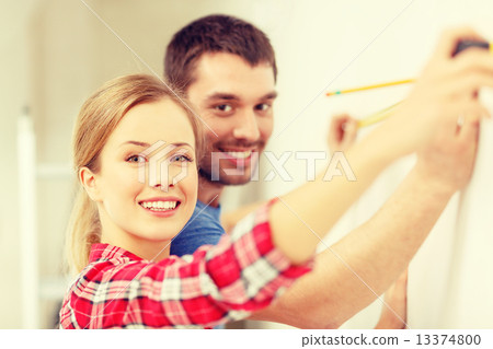 smiling couple measuring wall 13374800