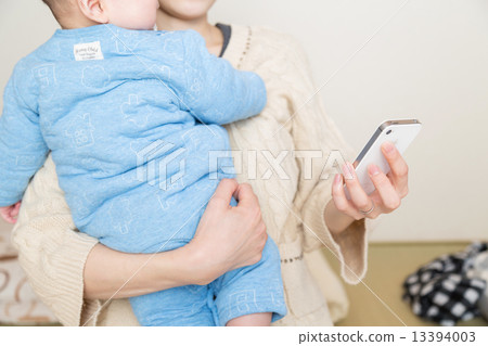 A woman looking at a smartphone holding a baby 13394003