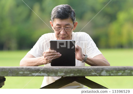 One male chinese elderly using iPad in the park One male chinese elderly using iPad in the park 13396529