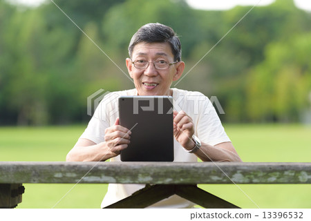 One male chinese elderly using iPad in the park 13396532