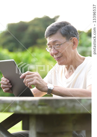 One male chinese elderly using iPad in the park 13396537