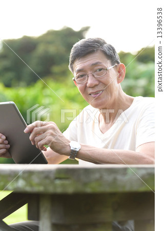 One male chinese elderly using iPad in the park 13396538