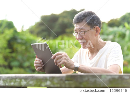 One male chinese elderly using iPad in the park 13396546