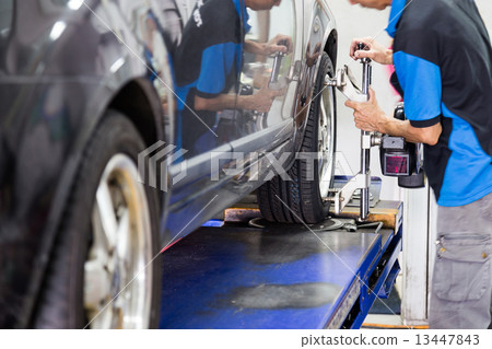 Mechanic fixing a wheel alignment device onto the wheel of a car 13447843
