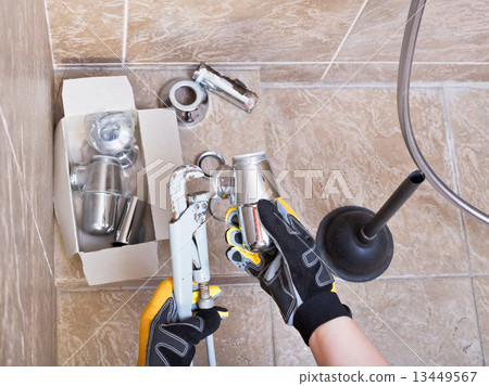plumber repairs sink trap in bathroom 13449567