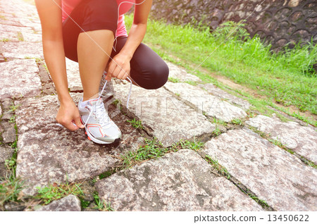 young woman runner tying shoelaces on stone trail young woman runner tying shoelaces on stone trail 13450622