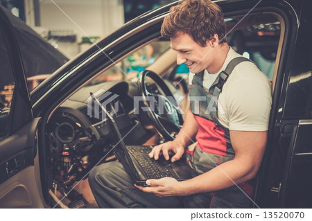 Serviceman making car diagnostics with laptop in a workshop Serviceman making car diagnostics with laptop in a workshop 13520070