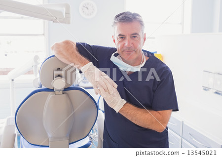 Smiling dentist leaning against dentists chair Smiling dentist leaning against dentists chair 13545021