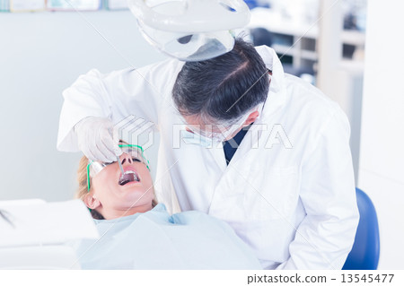 Dentist examining a patients teeth in the dentists chair 13545477