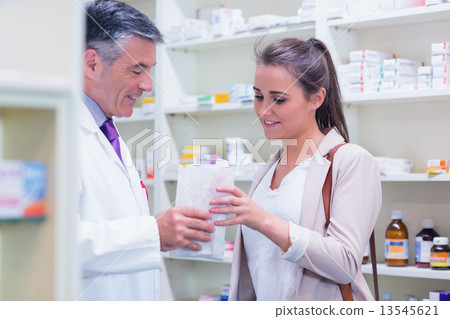 Pharmacist giving paper bag to his customer Pharmacist giving paper bag to his customer 13545621