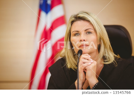 Portrait of a serious judge with american flag behind her 13545766
