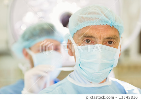 Stock Photo: Young surgeon tying older surgeons mask