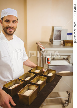 Happy baker holding tray of loaf tins 13545861
