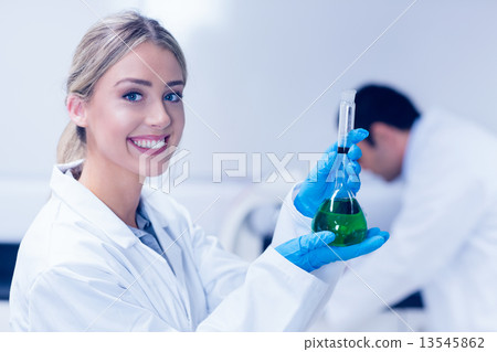 Science student holding green chemical in beaker 13545862