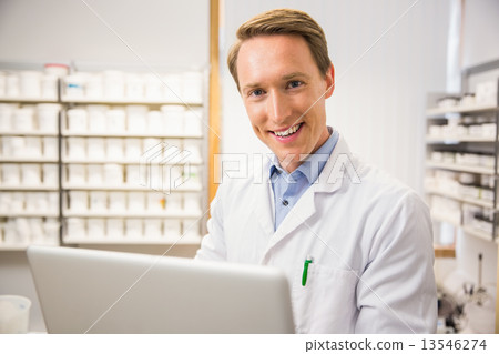 Happy pharmacist using his laptop 13546274