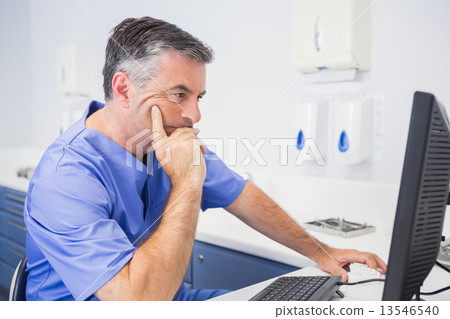 Serious dentist sitting and using computer 13546540