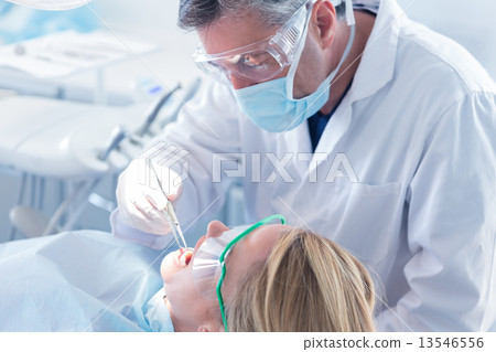 Dentist examining a patients teeth with surgical mask and gloves Dentist examining a patients teeth with surgical mask and gloves 13546556