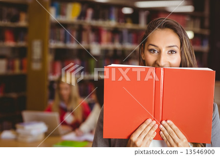 Pretty brunette student holding book in front of her face 13546900