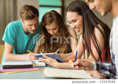 Smiling friends sitting studying and using tablet pc Smiling friends sitting studying and using tablet pc 13547649