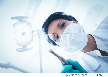 Female dentist in surgical mask holding dental drill 13547663