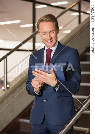 Handsome businessman standing on steps using tablet 13547863