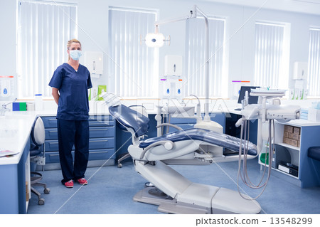 Dentist in blue scrubs standing beside chair Dentist in blue scrubs standing beside chair 13548299