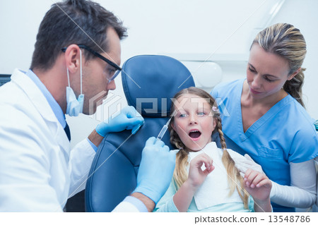 Dentist with assistant examining girls teeth 13548786