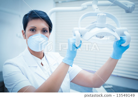 Demale dentist in surgical mask adjusting light 13549149
