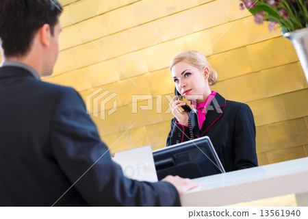 Hotel receptionist with phone and guest 13561940