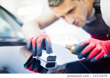 Worker on a car wash applying nano coating on a bonnet Worker on a car wash applying nano coating on a bonnet 13572676