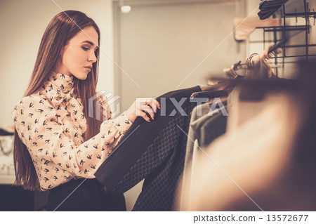 Young woman choosing clothes on a rack in a showroom Young woman choosing clothes on a rack in a showroom 13572677