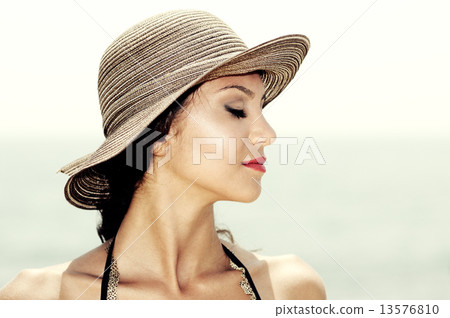 Attractive woman with a sun hat on a tropical beach, eyes closed 13576810