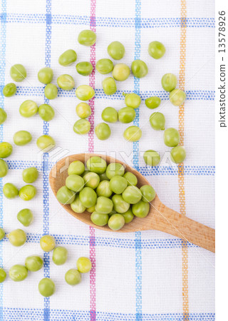 Green peas in a wooden spoon on the tablecloth. 13578926