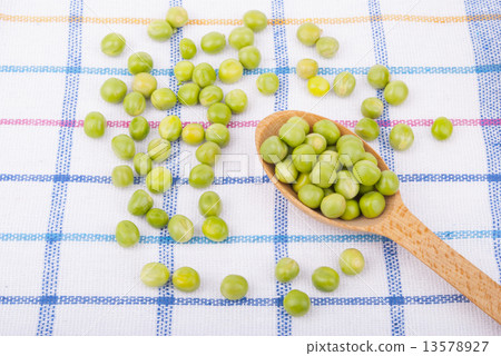 Green peas in a wooden spoon on the tablecloth. 13578927