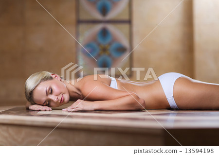 young woman lying on hammam table in turkish bath 13594198