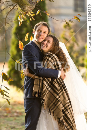 smiling bride and groom hugging under plaid at autumn park smiling bride and groom hugging under plaid at autumn park 13604239