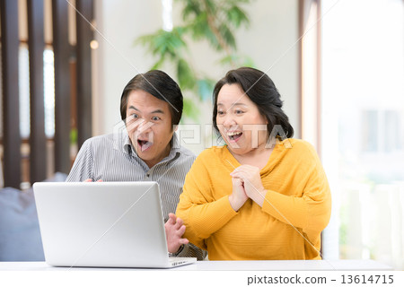 一對穿著休閒服的中年夫婦，他在自己的起居室裡操作一台個人電腦 13614715