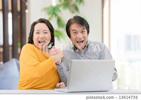 一對穿著休閒服的中年夫婦，他在自己的起居室裡操作一台個人電腦 13614738