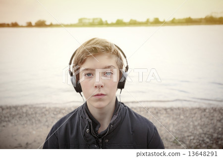 portrait of a teenage boy with headphones at a riverbank, toned 13648291