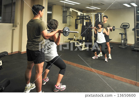 Asian woman is been guided by her male personal trainer during workout in indoor gym Asian woman is been guided by her male personal trainer during workout in indoor gym 13650600