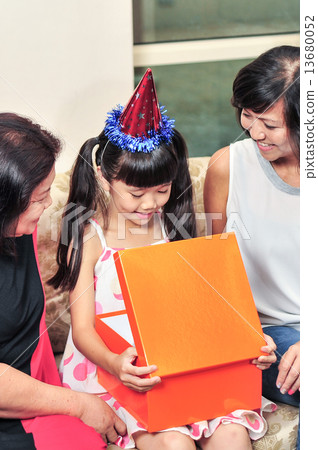 young Asian girl opening her present infront of her family during her birthday party young Asian girl opening her present infront of her family during her birthday party 13680052