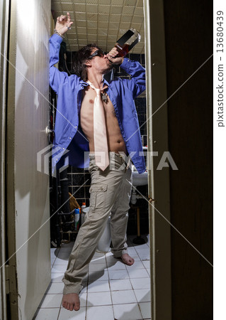Drunk Man is standing in a toilet with a bottle of whiskey Drunk Man is standing in a toilet with a bottle of whiskey 13680439