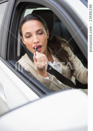 Pretty businesswoman using wing mirror to put on lipstick Pretty businesswoman using wing mirror to put on lipstick 13686196