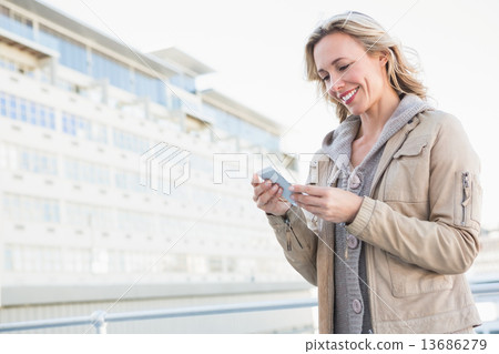 Smiling blonde standing and text messaging Smiling blonde standing and text messaging 13686279