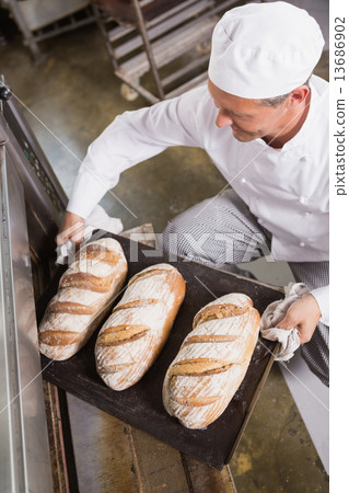 Baker taking tray of fresh bread out of oven Baker taking tray of fresh bread out of oven 13686902